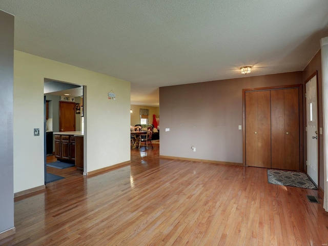 unfurnished living room with baseboards, light wood-style flooring, visible vents, and a textured ceiling