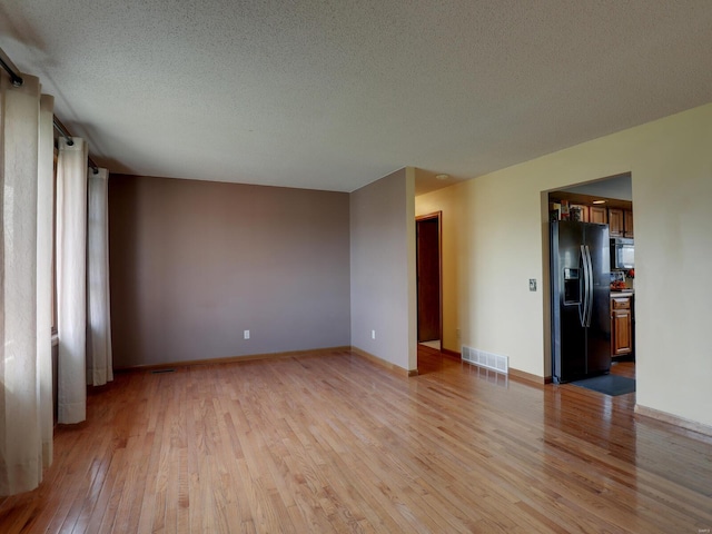 unfurnished room featuring a textured ceiling, baseboards, visible vents, and light wood-style floors