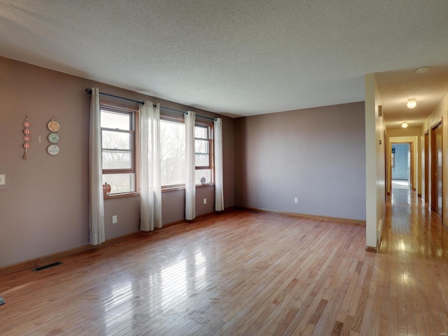 spare room featuring a textured ceiling, visible vents, light wood-style flooring, and baseboards