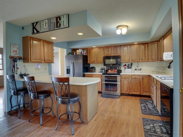 kitchen with a peninsula, light countertops, light wood-type flooring, black appliances, and a kitchen bar