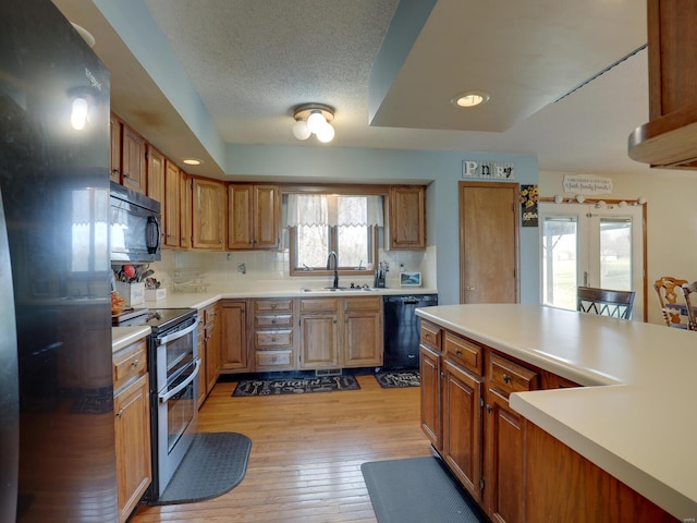 kitchen featuring brown cabinets, black appliances, light countertops, and a sink