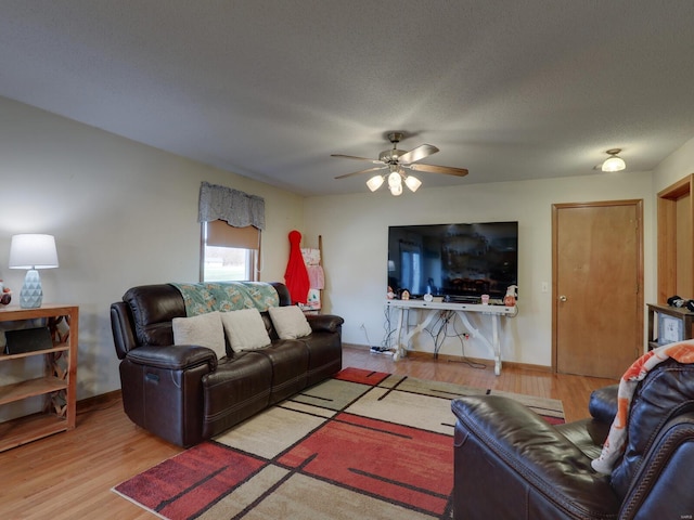 living area featuring light wood-style flooring, baseboards, ceiling fan, and a textured ceiling