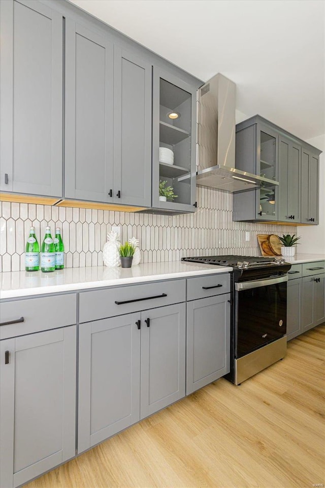 kitchen featuring backsplash, light hardwood / wood-style flooring, wall chimney exhaust hood, and stainless steel range oven