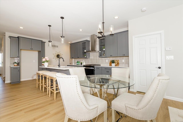 kitchen with pendant lighting, wall chimney exhaust hood, gray cabinets, and stainless steel stove