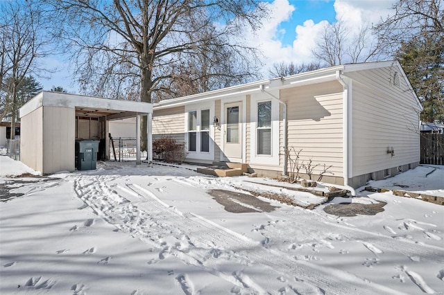 snow covered back of property featuring a carport, entry steps, and a garage