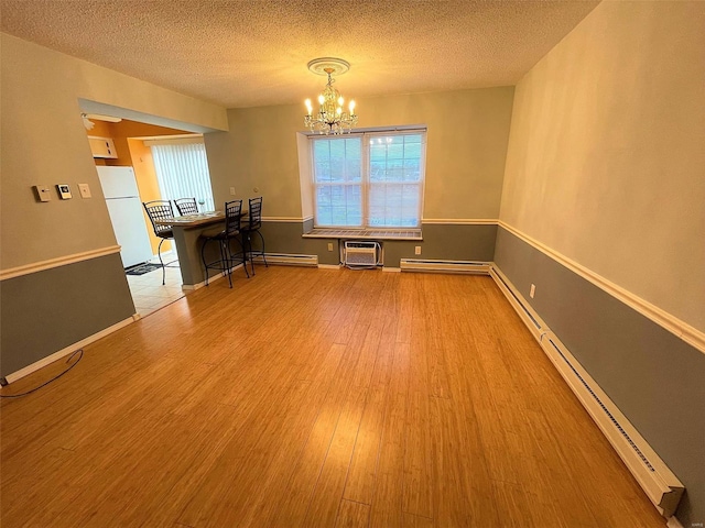 unfurnished dining area featuring light wood-type flooring, a textured ceiling, baseboard heating, an inviting chandelier, and an AC wall unit