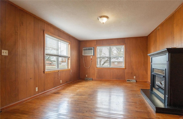 unfurnished living room with a textured ceiling, wood walls, light hardwood / wood-style floors, and a wall mounted air conditioner