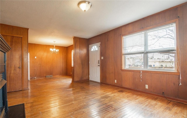 entryway featuring a textured ceiling, wooden walls, a notable chandelier, and light wood-type flooring