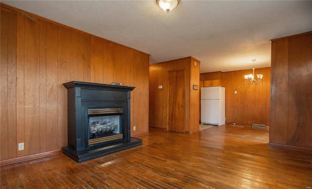 unfurnished living room with hardwood / wood-style floors, wood walls, a textured ceiling, and a chandelier