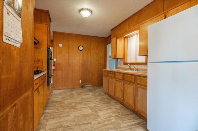 kitchen featuring wood walls, sink, a textured ceiling, and white refrigerator