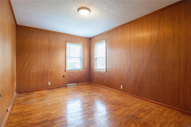 spare room with wooden walls, wood-type flooring, and a textured ceiling