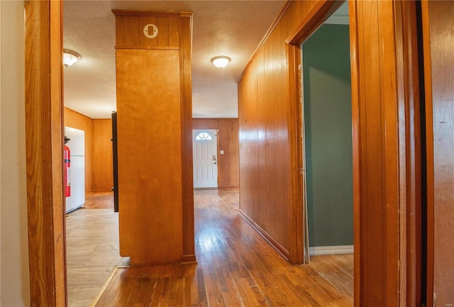 hall with hardwood / wood-style floors, a textured ceiling, and wooden walls