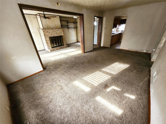 unfurnished living room with dark colored carpet, ceiling fan, and a brick fireplace