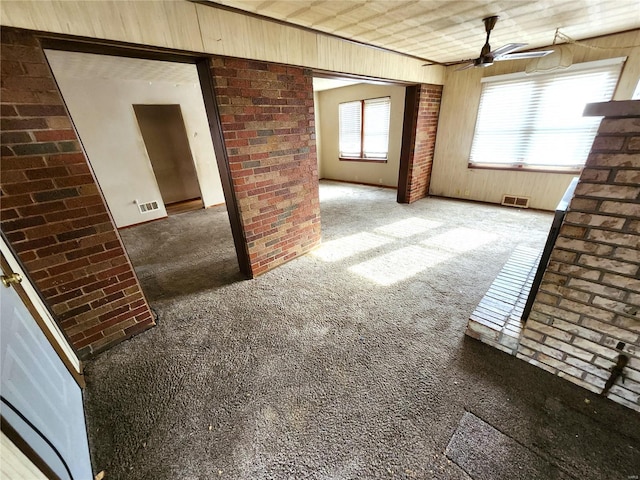 unfurnished living room featuring carpet floors, ceiling fan, wooden walls, and brick wall