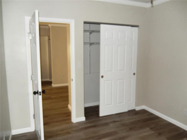 unfurnished bedroom featuring dark hardwood / wood-style flooring, crown molding, and a closet