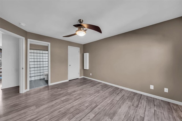 unfurnished bedroom featuring ceiling fan, ensuite bath, wood finished floors, and baseboards