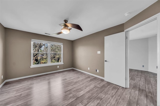 empty room with ceiling fan, visible vents, baseboards, and wood finished floors