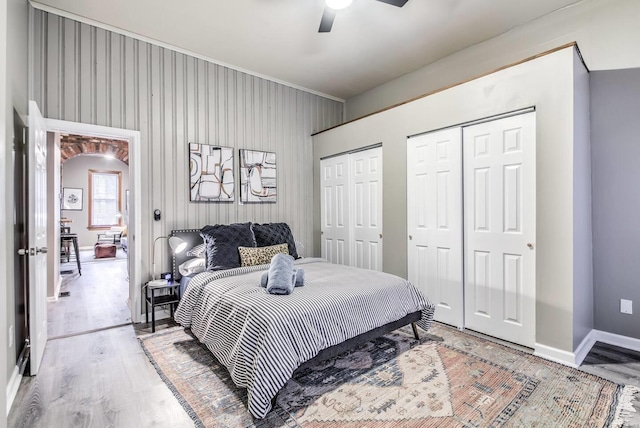 bedroom featuring hardwood / wood-style flooring, ceiling fan, and multiple closets