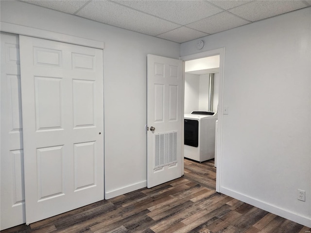 unfurnished bedroom featuring a closet, a drop ceiling, dark hardwood / wood-style floors, and washer / dryer