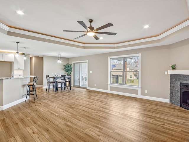 unfurnished living room with a raised ceiling, a fireplace, crown molding, and light hardwood / wood-style flooring