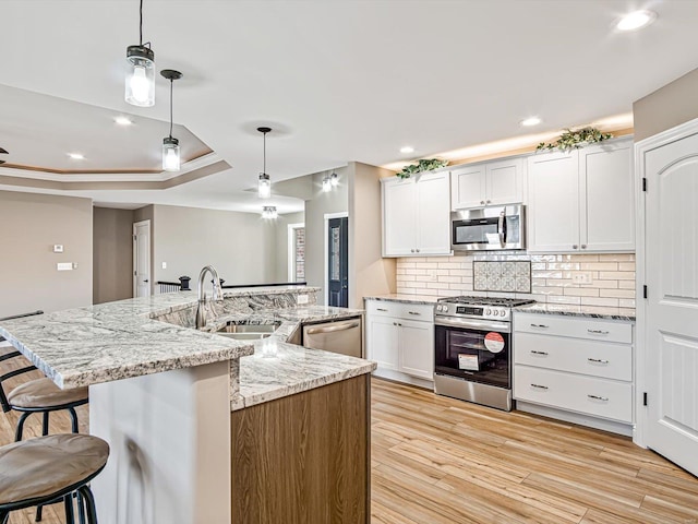 kitchen with decorative light fixtures, stainless steel appliances, white cabinetry, and a center island with sink