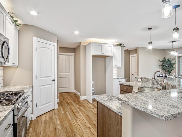 kitchen featuring light wood-type flooring, stainless steel appliances, sink, white cabinets, and hanging light fixtures