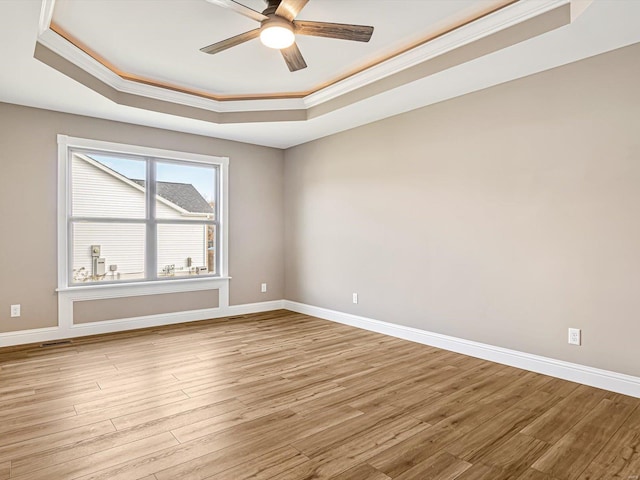 spare room with light wood-type flooring, a tray ceiling, ceiling fan, and ornamental molding