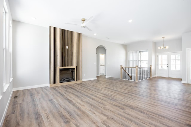 unfurnished living room with ceiling fan with notable chandelier and light hardwood / wood-style flooring