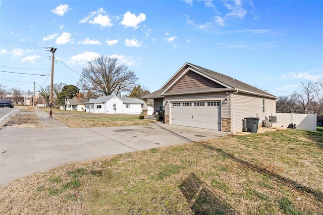 view of side of property with stone siding, fence, concrete driveway, and a yard