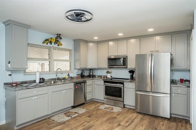 kitchen featuring gray cabinetry, sink, stainless steel appliances, dark stone counters, and light hardwood / wood-style floors