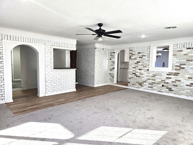 empty room with dark colored carpet, brick wall, ceiling fan, and a textured ceiling