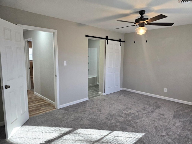 unfurnished bedroom featuring a barn door, carpet flooring, connected bathroom, and ceiling fan