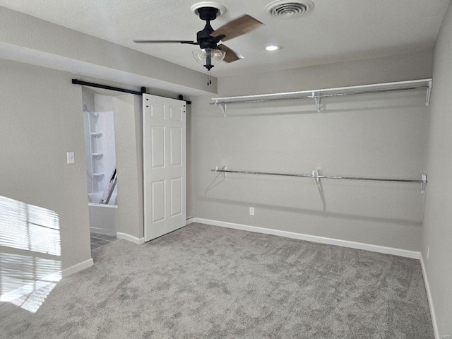 spacious closet with ceiling fan, light colored carpet, and a barn door