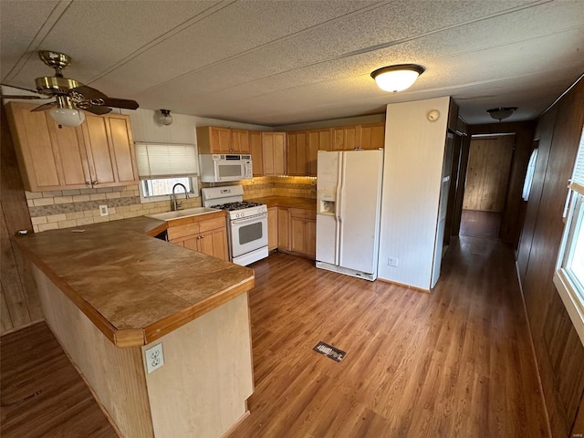 kitchen with kitchen peninsula, light wood-type flooring, tasteful backsplash, white appliances, and sink