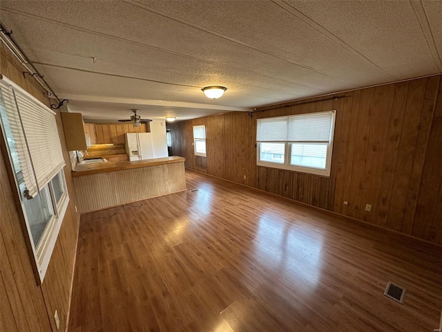 unfurnished living room with ceiling fan, wood walls, a textured ceiling, and light hardwood / wood-style flooring