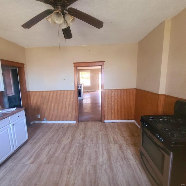 kitchen featuring gas range, white cabinetry, ceiling fan, wood walls, and light wood-type flooring