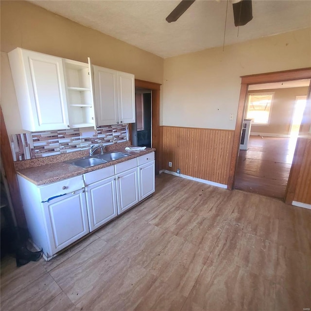 kitchen with white cabinetry, sink, wooden walls, and light hardwood / wood-style flooring