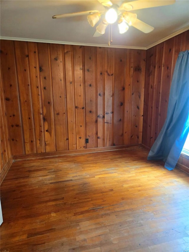 empty room with wooden walls, crown molding, ceiling fan, and light wood-type flooring