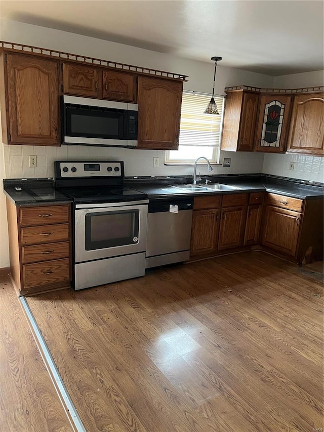 kitchen featuring sink, light wood-type flooring, tasteful backsplash, decorative light fixtures, and stainless steel appliances