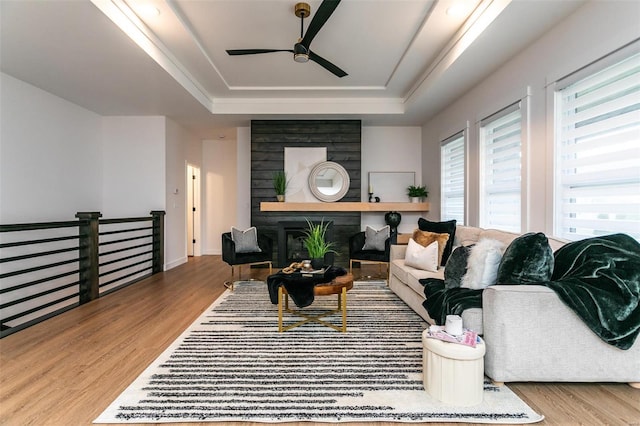 living room with a raised ceiling, ceiling fan, a large fireplace, and wood-type flooring