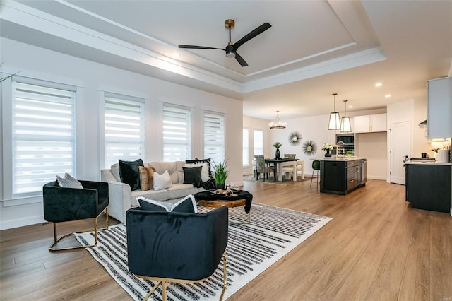 living room featuring a raised ceiling, ceiling fan with notable chandelier, and light wood-type flooring