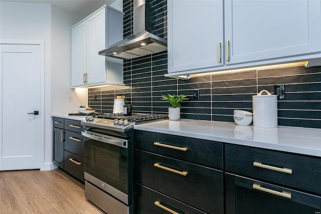 kitchen with white cabinetry, wall chimney exhaust hood, stainless steel gas range, decorative backsplash, and light wood-type flooring