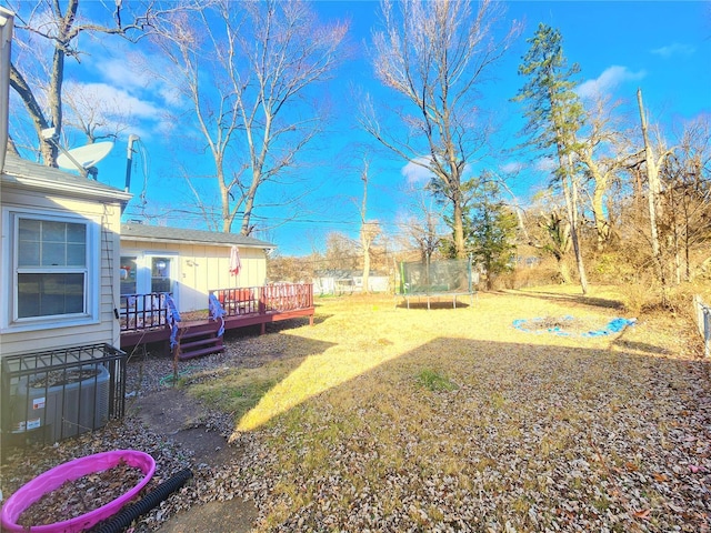 view of yard featuring a deck, central AC unit, and a trampoline