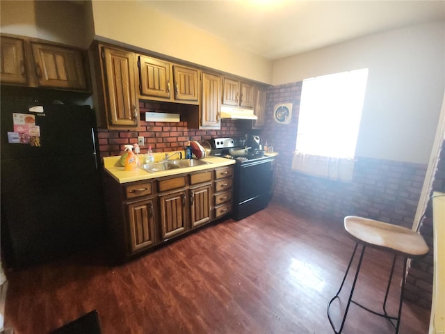 kitchen with dark wood-style flooring, under cabinet range hood, light countertops, black appliances, and a sink