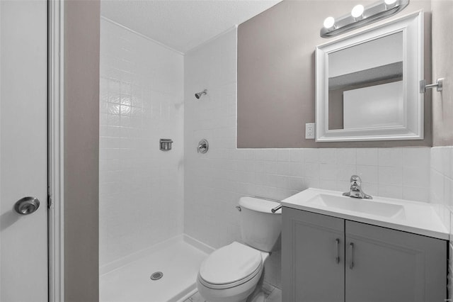 bathroom featuring a tile shower, a textured ceiling, toilet, vanity, and tile walls