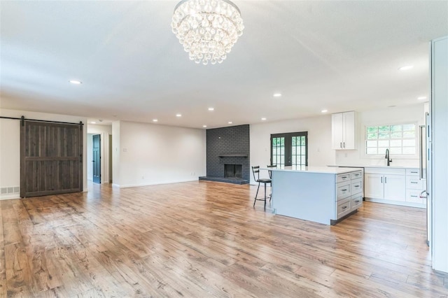 unfurnished living room featuring french doors, an inviting chandelier, a barn door, a fireplace, and light wood-type flooring