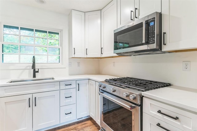 kitchen with sink, white cabinetry, stainless steel appliances, and light wood-type flooring