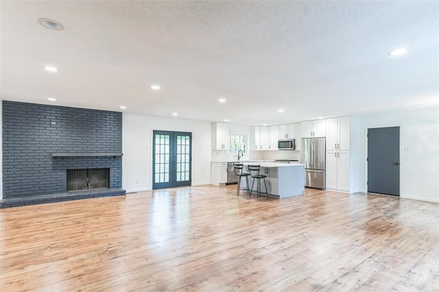 unfurnished living room with french doors, a textured ceiling, sink, light hardwood / wood-style flooring, and a fireplace