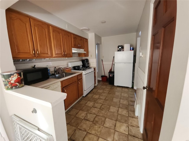 kitchen featuring white appliances, brown cabinets, light countertops, under cabinet range hood, and a sink