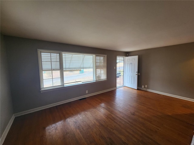 spare room featuring visible vents, baseboards, and dark wood finished floors